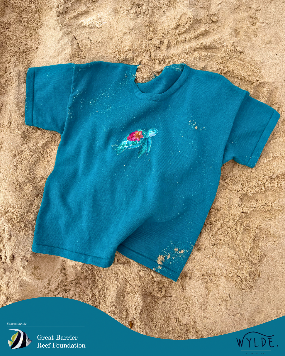Blue t-shirt with a design on a sandy background, featuring the Great Barrier Reef Foundation logo. Soft organic cotton kids t-shirt supporting reef conservation