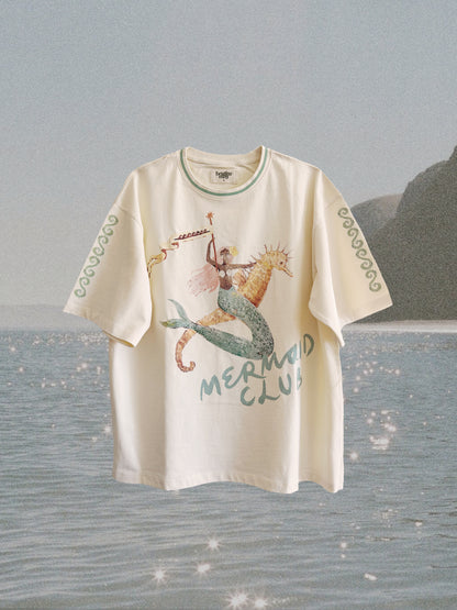 White t-shirt with mermaid design and 'Mermaid Club' text on a beach background