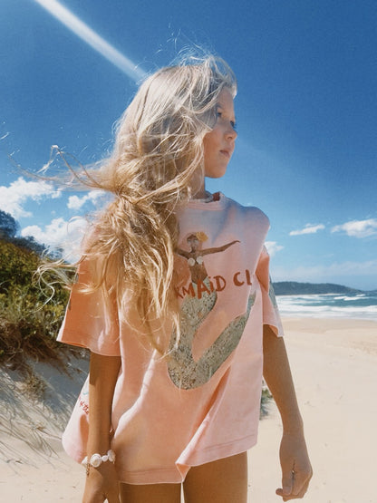 girl wearing a pink t-shirt with a hand illustrated mermaid artwork print on a beach